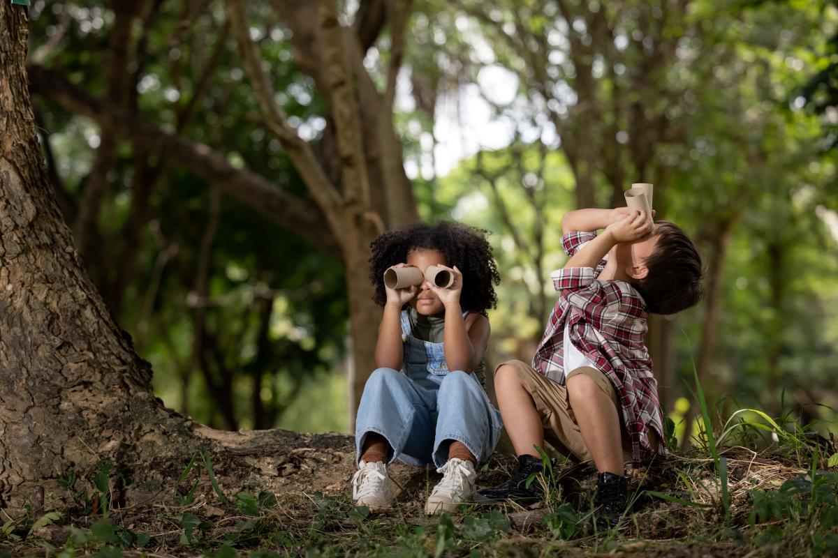 two children sitting in the woods looking through binoculars made from toilet paper rolls