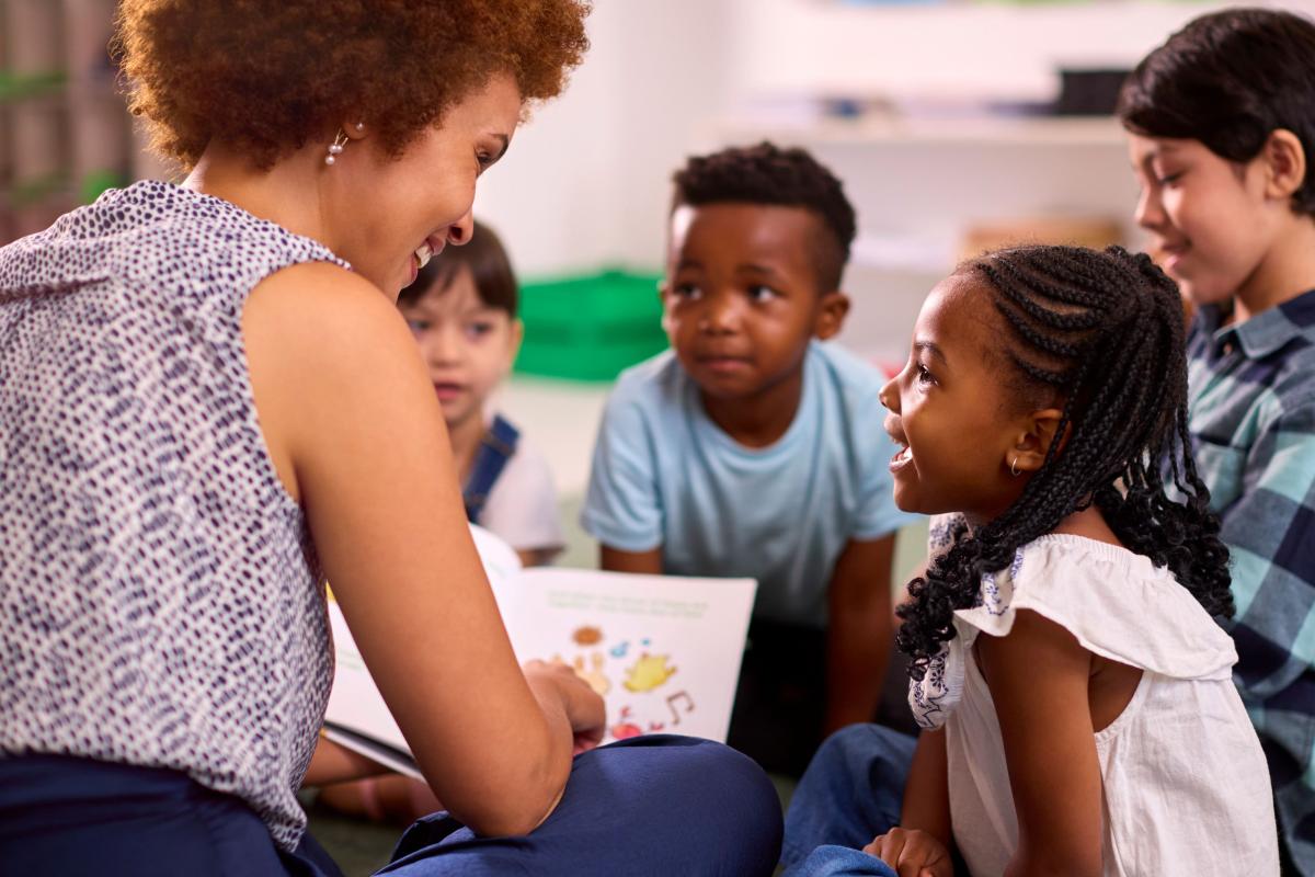 woman reads to a multi-ethnic group of children while sitting on the floor