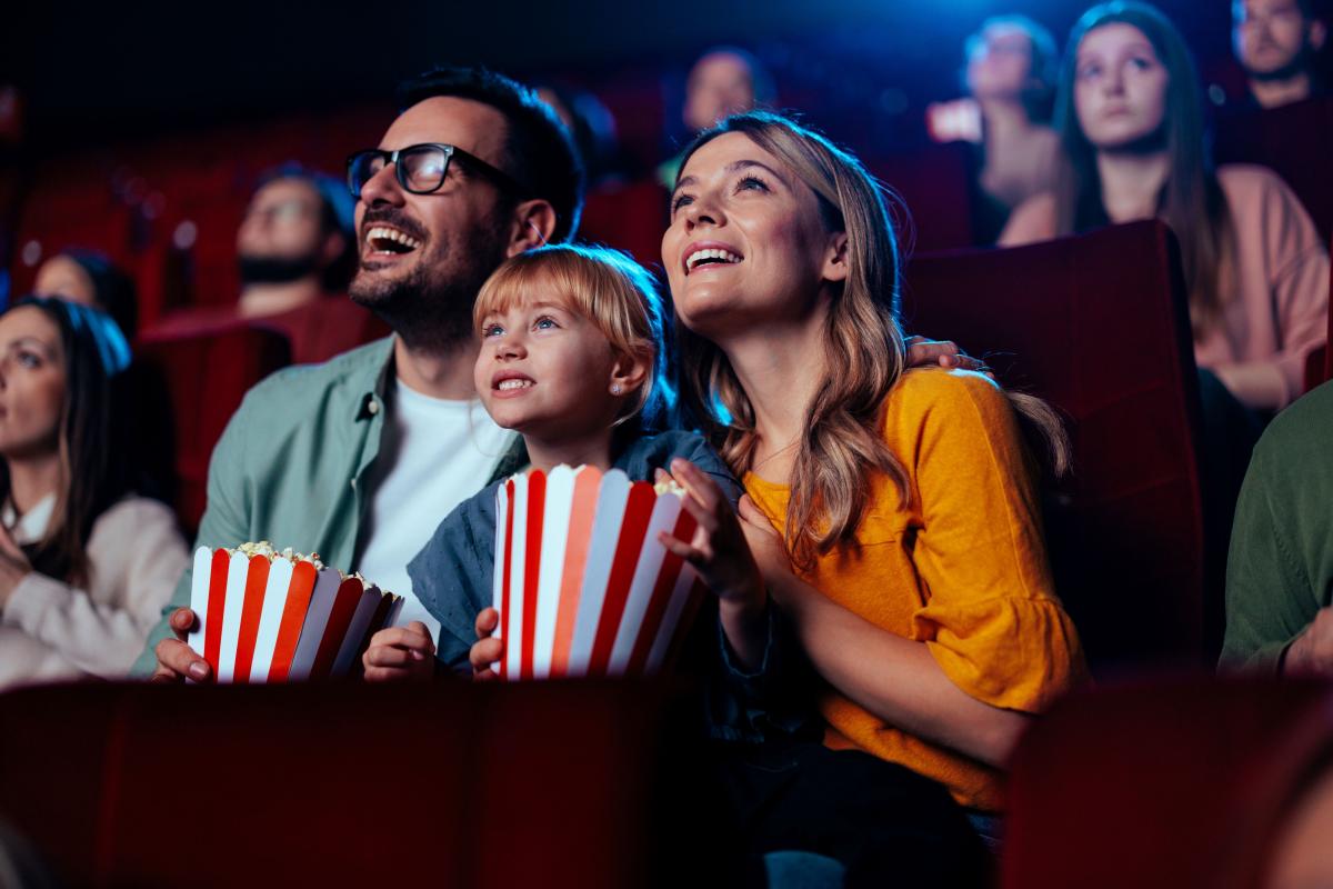 small child sits between a man and woman in a movie theater eating popcorn