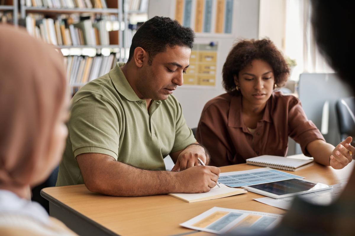 man sits next to a woman at a table while taking notes