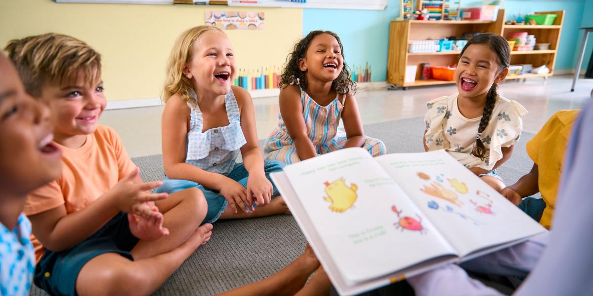 person reading a story to a group of children facing them laughing