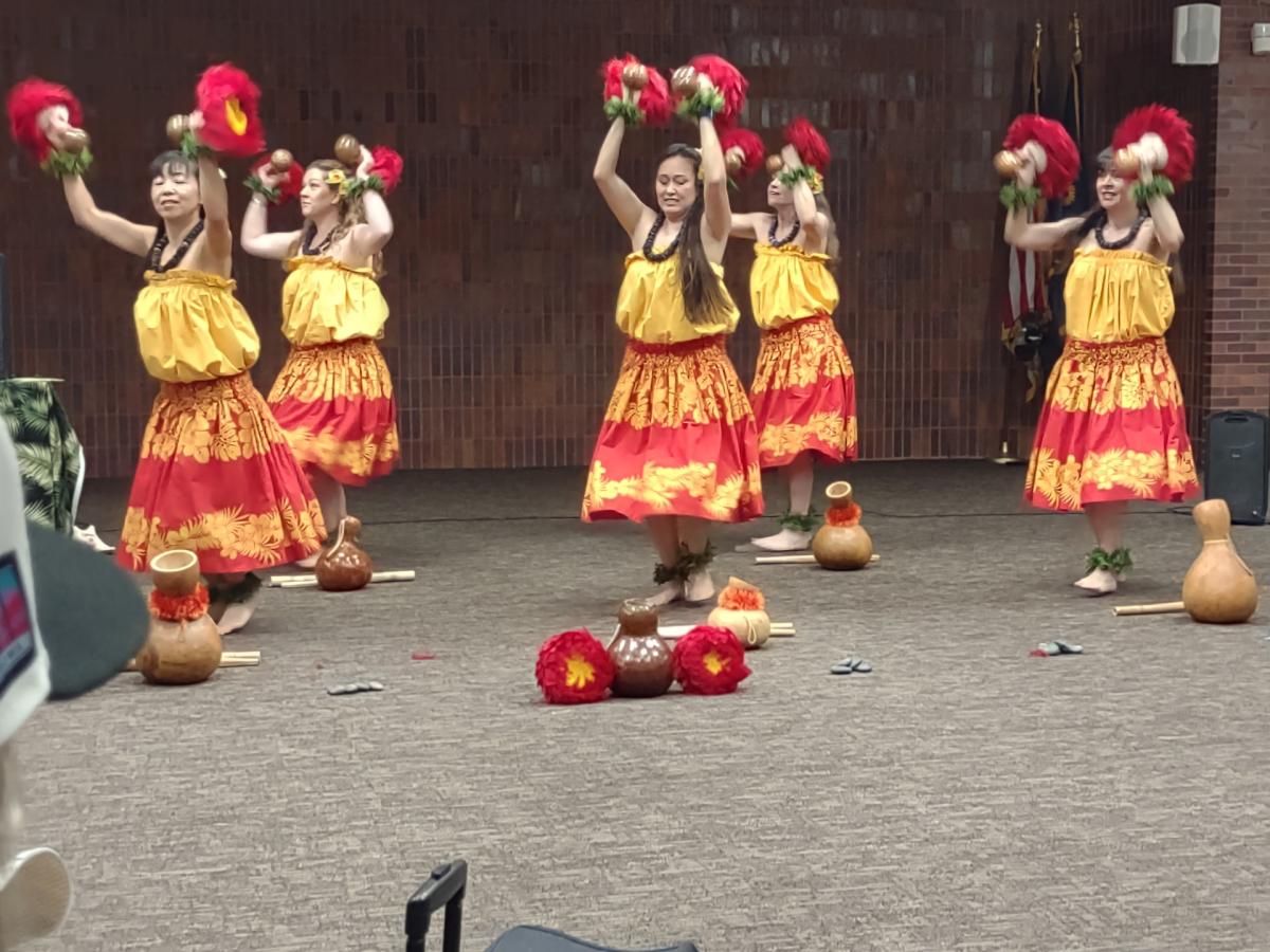 Hawaiian dancers in yellow, orange, and red dresses; arms in the air dancing