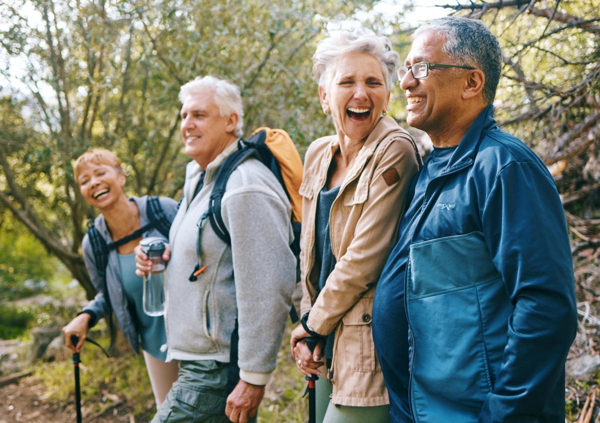 Four older adults laugh with one another while hiking. 