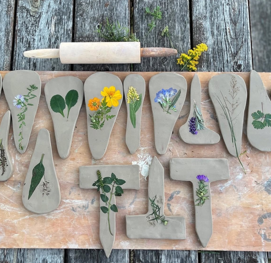 flattened clay works with flowers and plants inside, laying on a wooden table, below a rolling pin