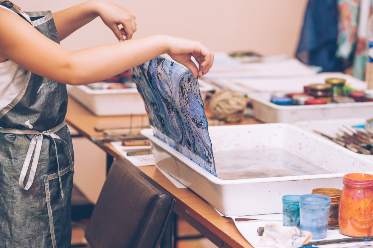 teen lifting paper off water where ink has been swirled to create a design the paper