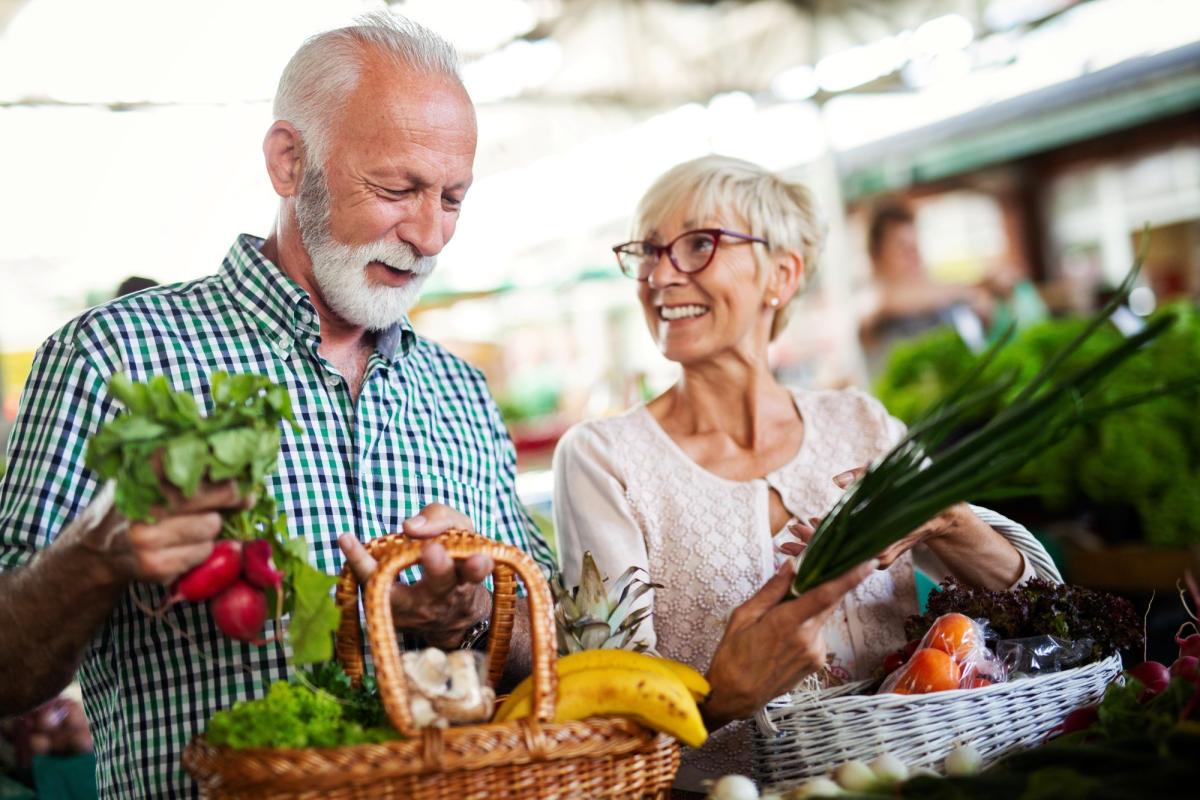 2 older adults holding baskets of fresh fruits and vegetables smiling at each other