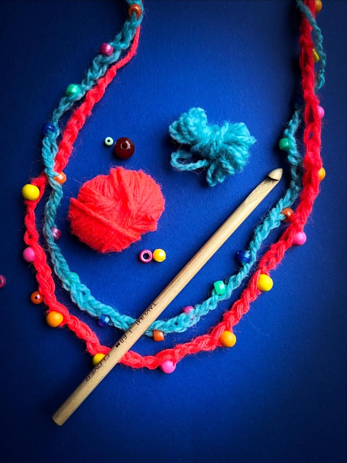 Red and Blue Crochet necklace with the balls of colored yarn next to them on a dark blue background