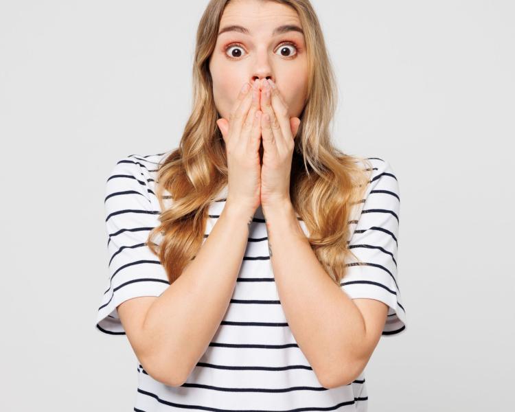 shocked woman in striped shirt with hands covering mouth