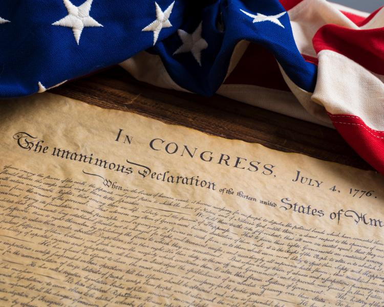 copy of declartion of independence laying on table with American flag laying above it. 