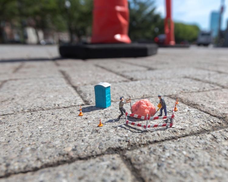 miniature people figurines on a brick sidewalk using construction equipment to remove a piece of bubble gum, image by Luke Pech