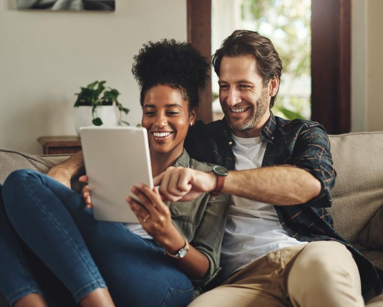 couple on a couch smiling and interacting with a tablet computer